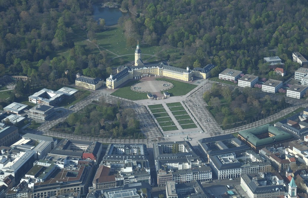 Luftbild von Karlsruhe: In der Mitte das gelbe Schloss mit Turm, dahinter der große grüne Schlossgarten. Davor der Schlossplatz, von dem die Straßen fächerförmig in die Stadt führen.
